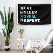 Load image into Gallery viewer, In a home setting, a flag with the saying &quot;Eat Sleep Swim Repeat&quot; is mounted on a white wall by a side table.
