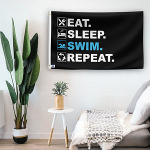 In a home setting, a flag with the saying "Eat Sleep Swim Repeat" is mounted on a white wall by a side table.