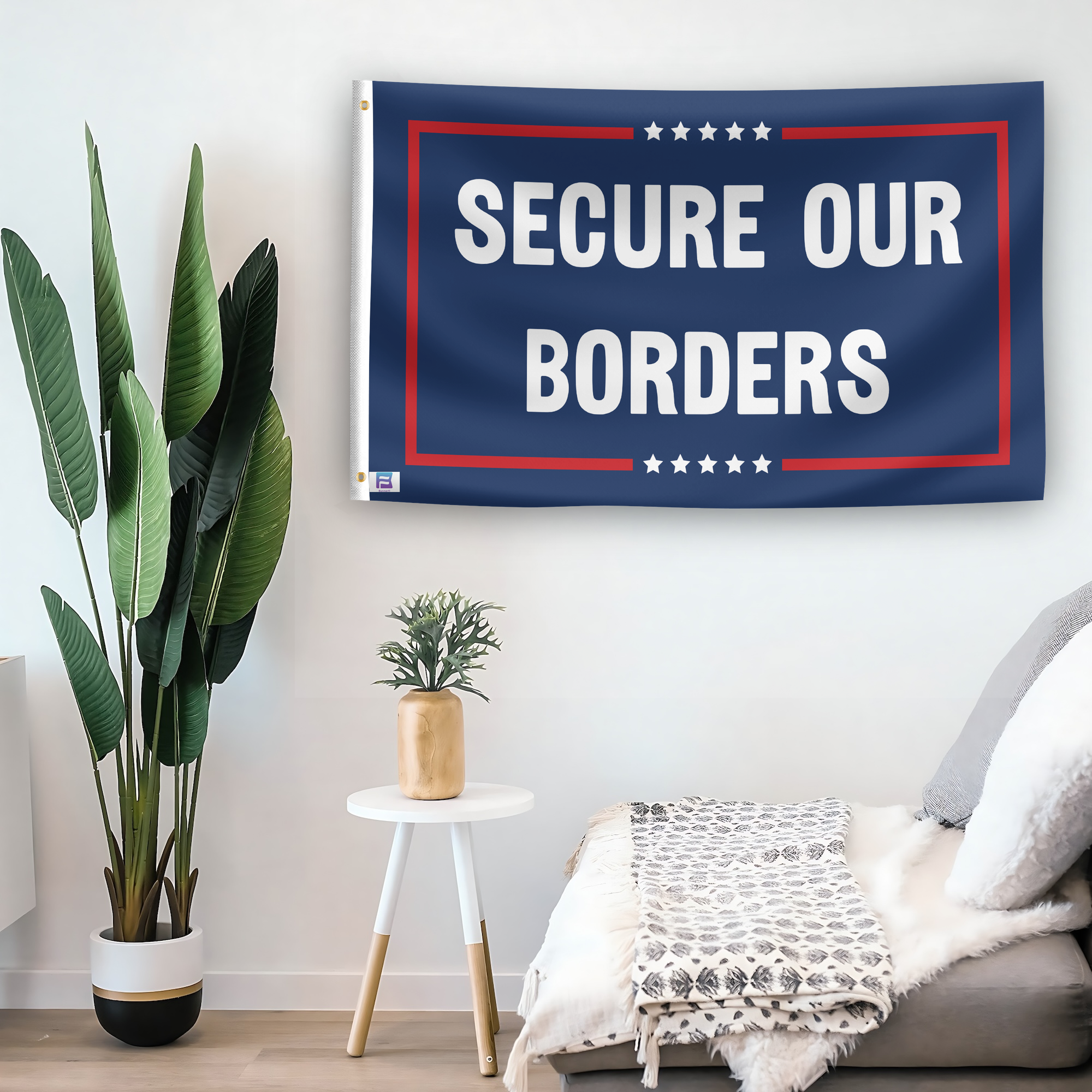 In a home setting, a flag with the saying "Secure Our Borders Political" is mounted on a white wall by a side table.