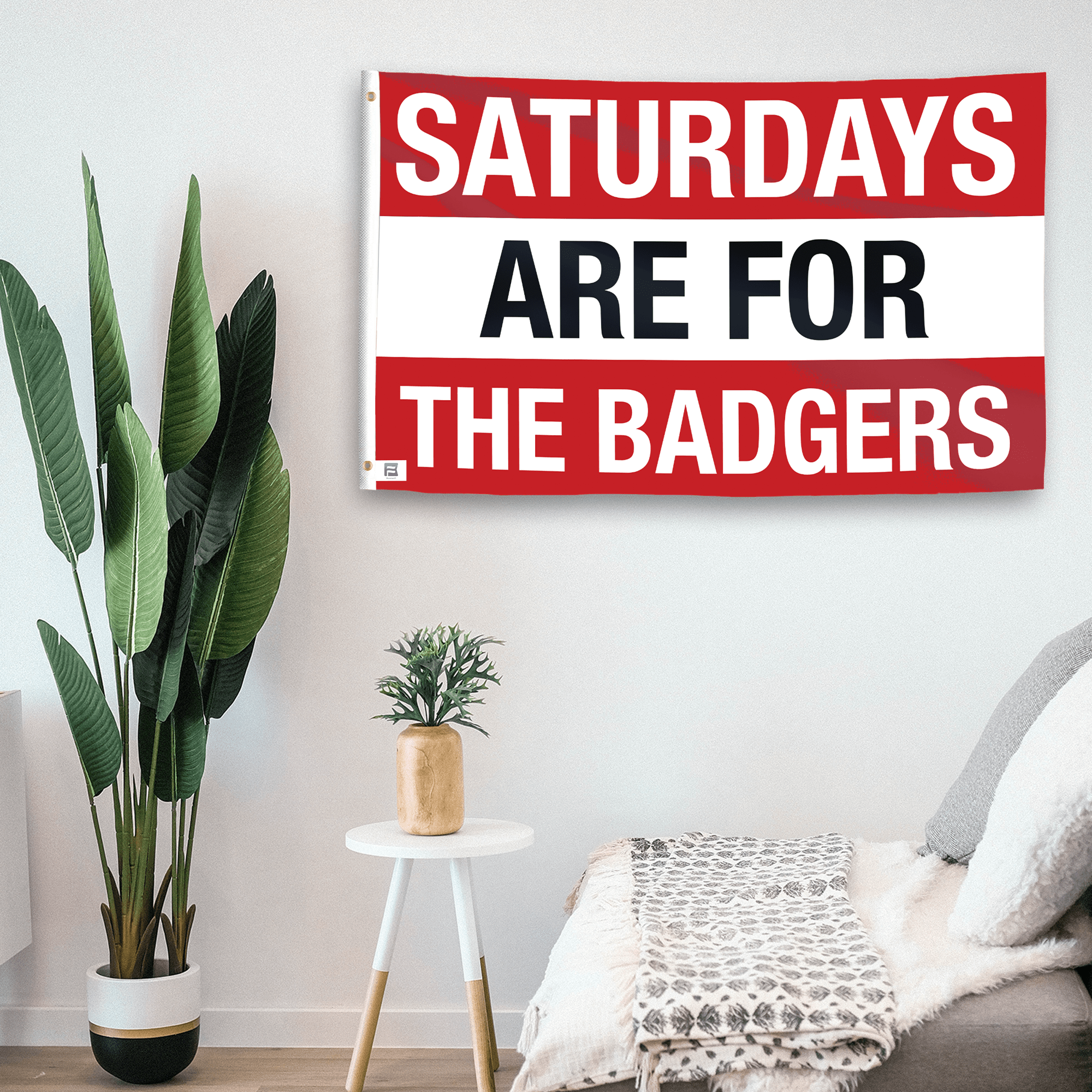 In a home setting, a flag with the saying "Saturdays Are for the Badgers" is mounted on a white wall by a side table.