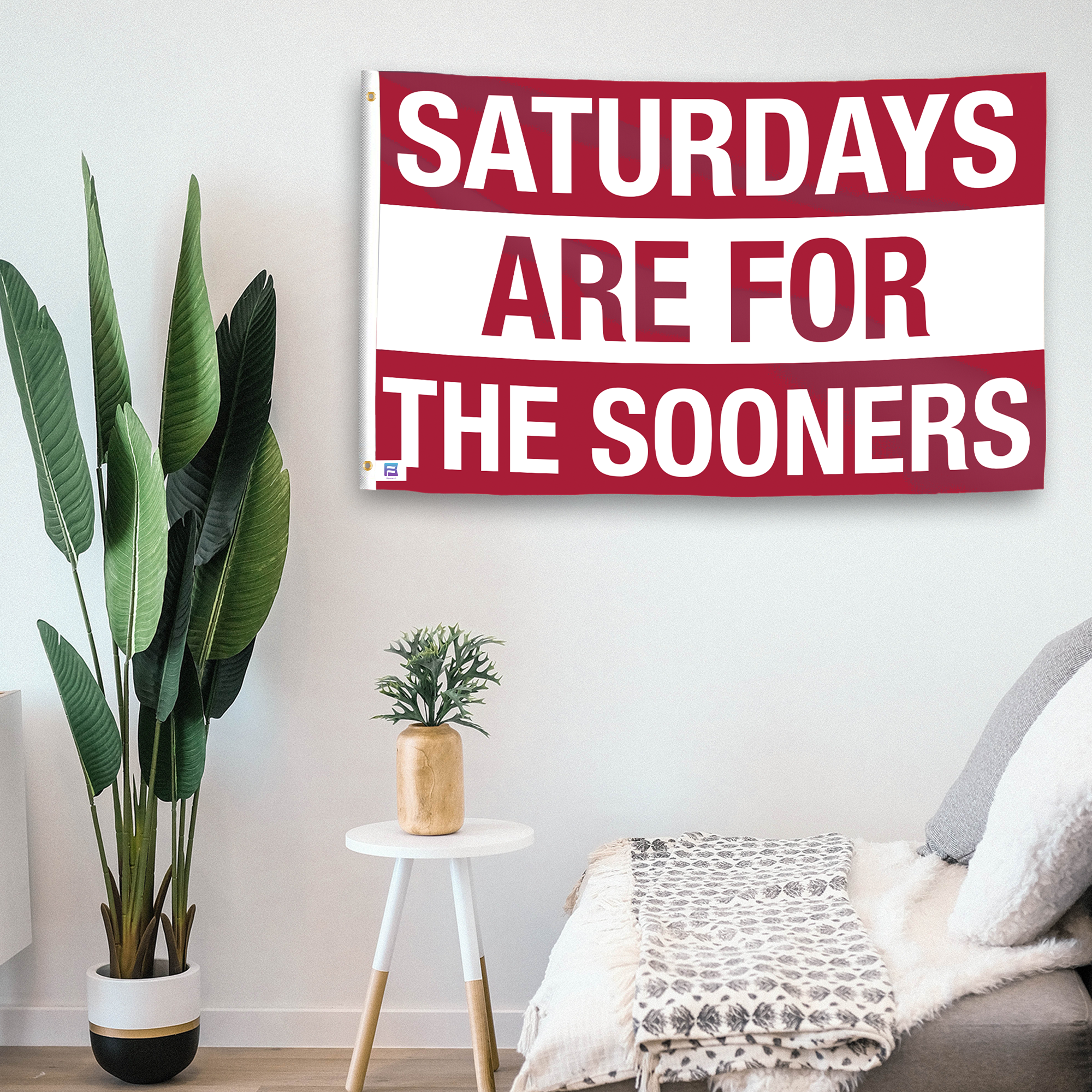 In a home setting, a flag with the saying "Saturdays Are for the Sooners" is mounted on a white wall by a side table.