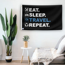 Load image into Gallery viewer, In a home setting, a flag with the saying &quot;Eat Sleep Travel Repeat&quot; is mounted on a white wall by a side table.
