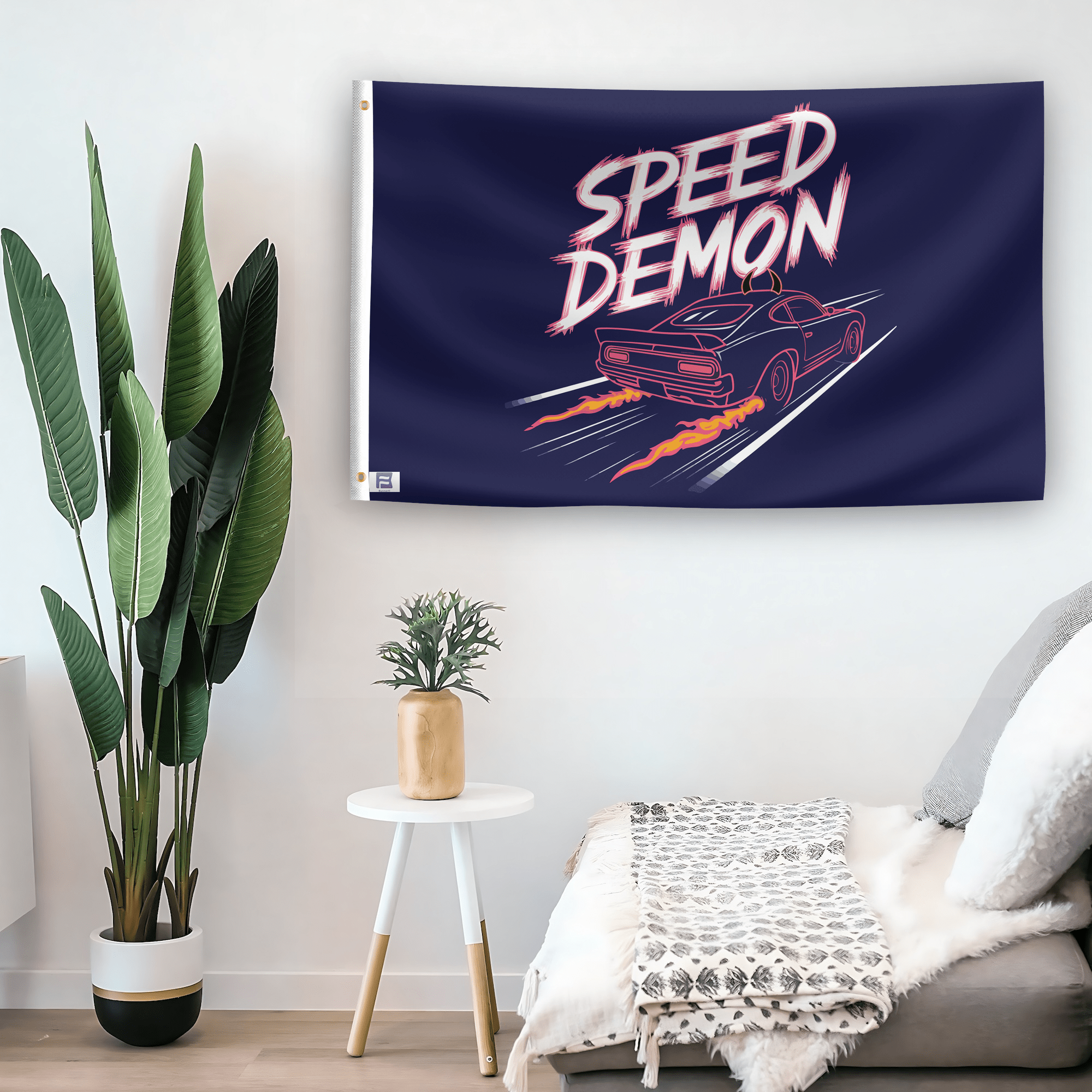 In a home setting, a flag with the saying "Speed Demon" is mounted on a white wall by a side table.