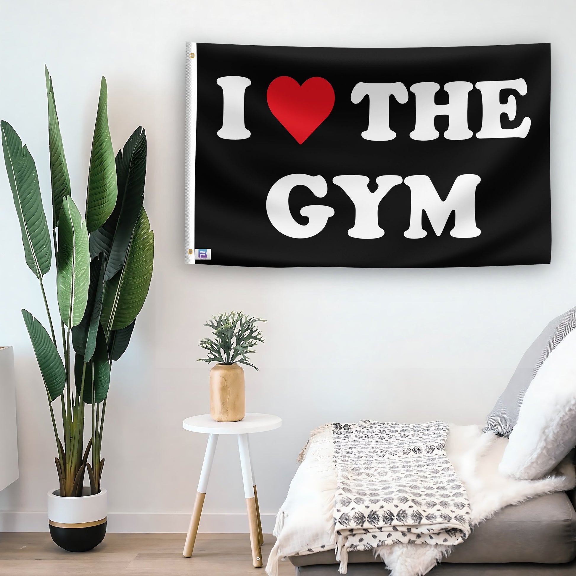 In a home setting, a flag with the saying "I Love The Gym" is mounted on a white wall by a side table.