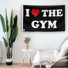 Load image into Gallery viewer, In a home setting, a flag with the saying &quot;I Love The Gym&quot; is mounted on a white wall by a side table.
