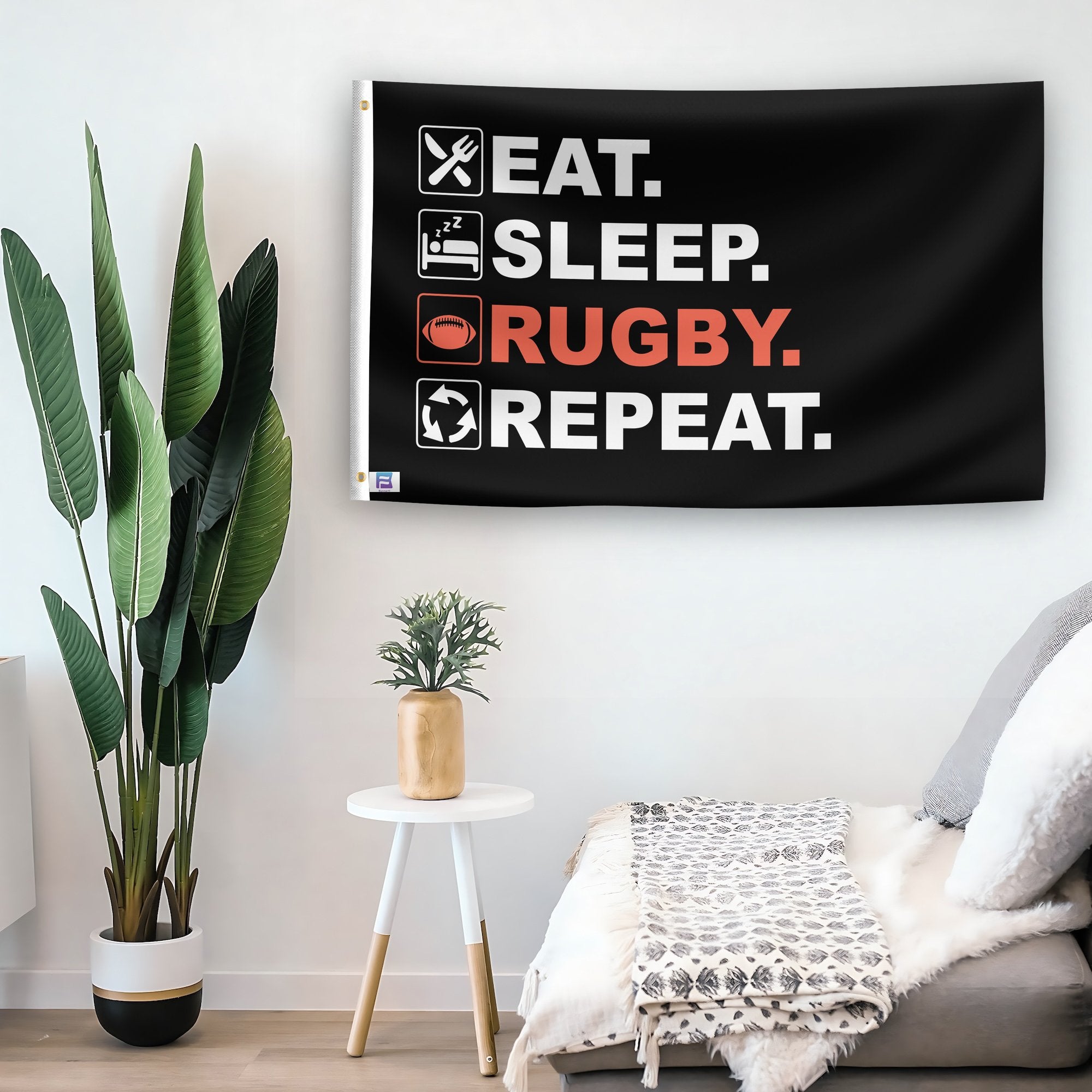 In a home setting, a flag with the saying "Eat Sleep Rugby Repeat" is mounted on a white wall by a side table.