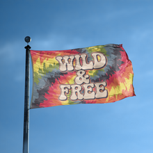 Load image into Gallery viewer, A flag with the saying &quot;Wild and Free&quot; displayed on a high pole, with a tie dye style color scheme.
