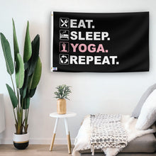 Load image into Gallery viewer, In a home setting, a flag with the saying &quot;Eat Sleep Yoga Repeat&quot; is mounted on a white wall by a side table.
