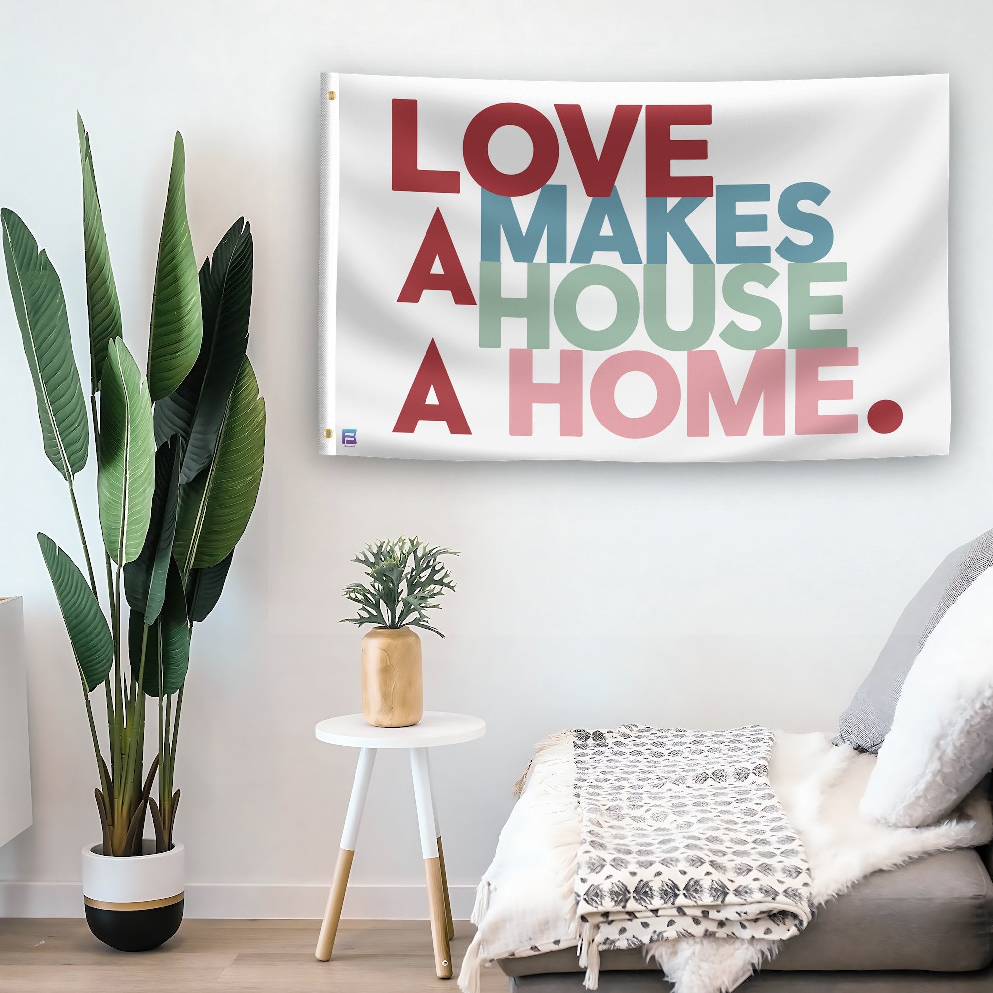 In a home setting, a flag with the saying "Love Makes A House A Home" is mounted on a white wall by a side table.