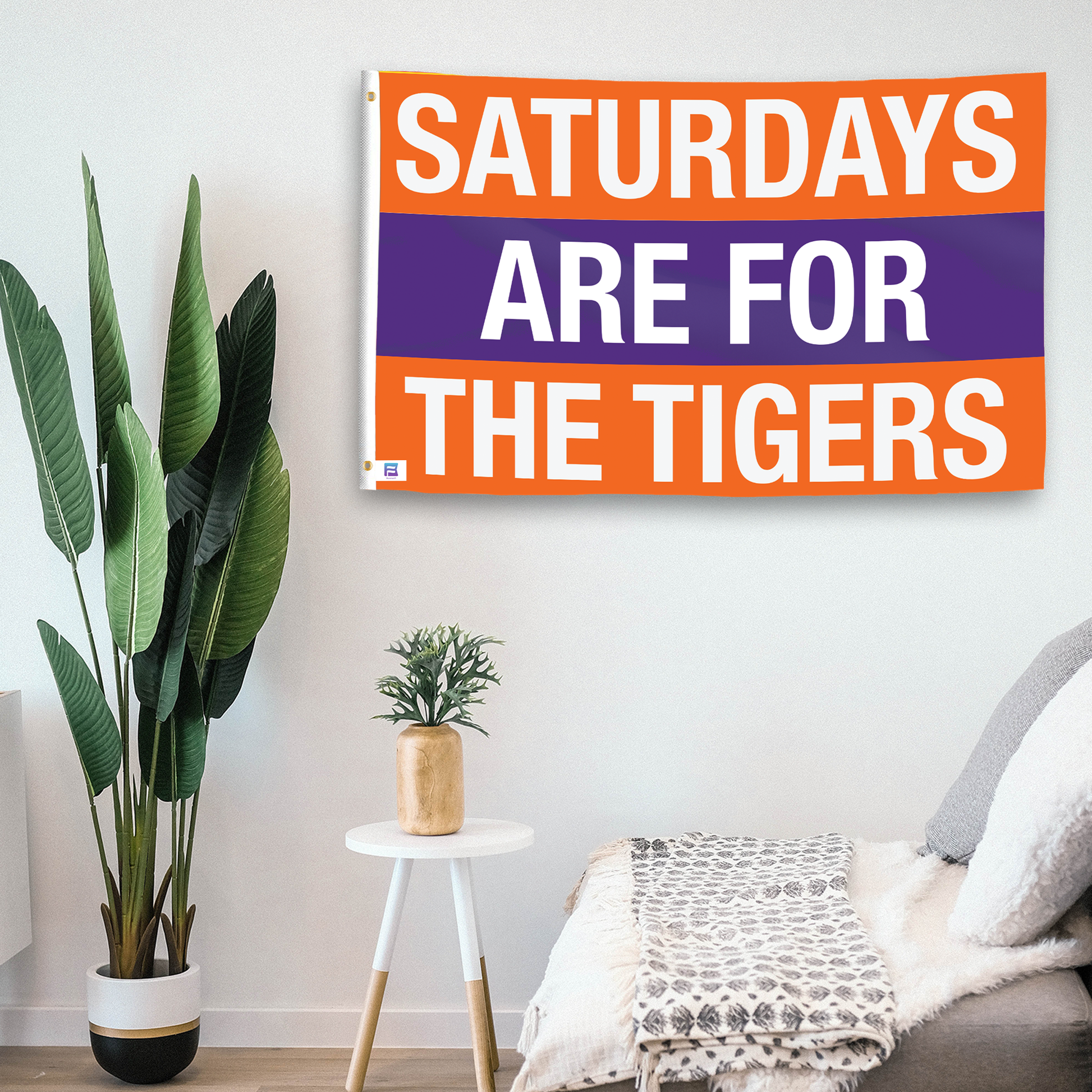 In a home setting, a flag with the saying "Saturdays Are for the Tigers Clemson" is mounted on a white wall by a side table.