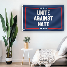 Load image into Gallery viewer, In a home setting, a flag with the saying &quot;Unite Against Hate Political&quot; is mounted on a white wall by a side table.
