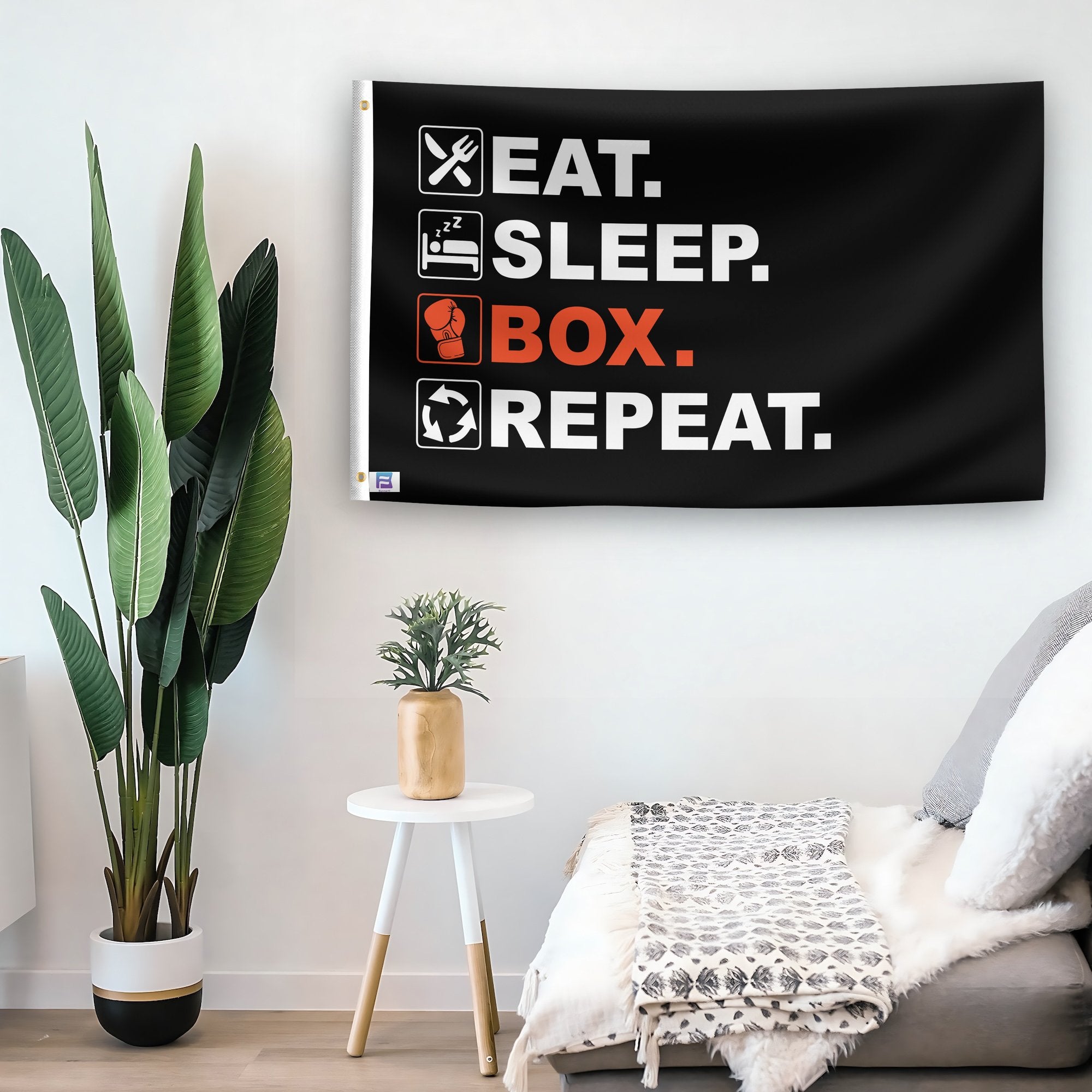 In a home setting, a flag with the saying "Eat Sleep Boxing Repeat" is mounted on a white wall by a side table.