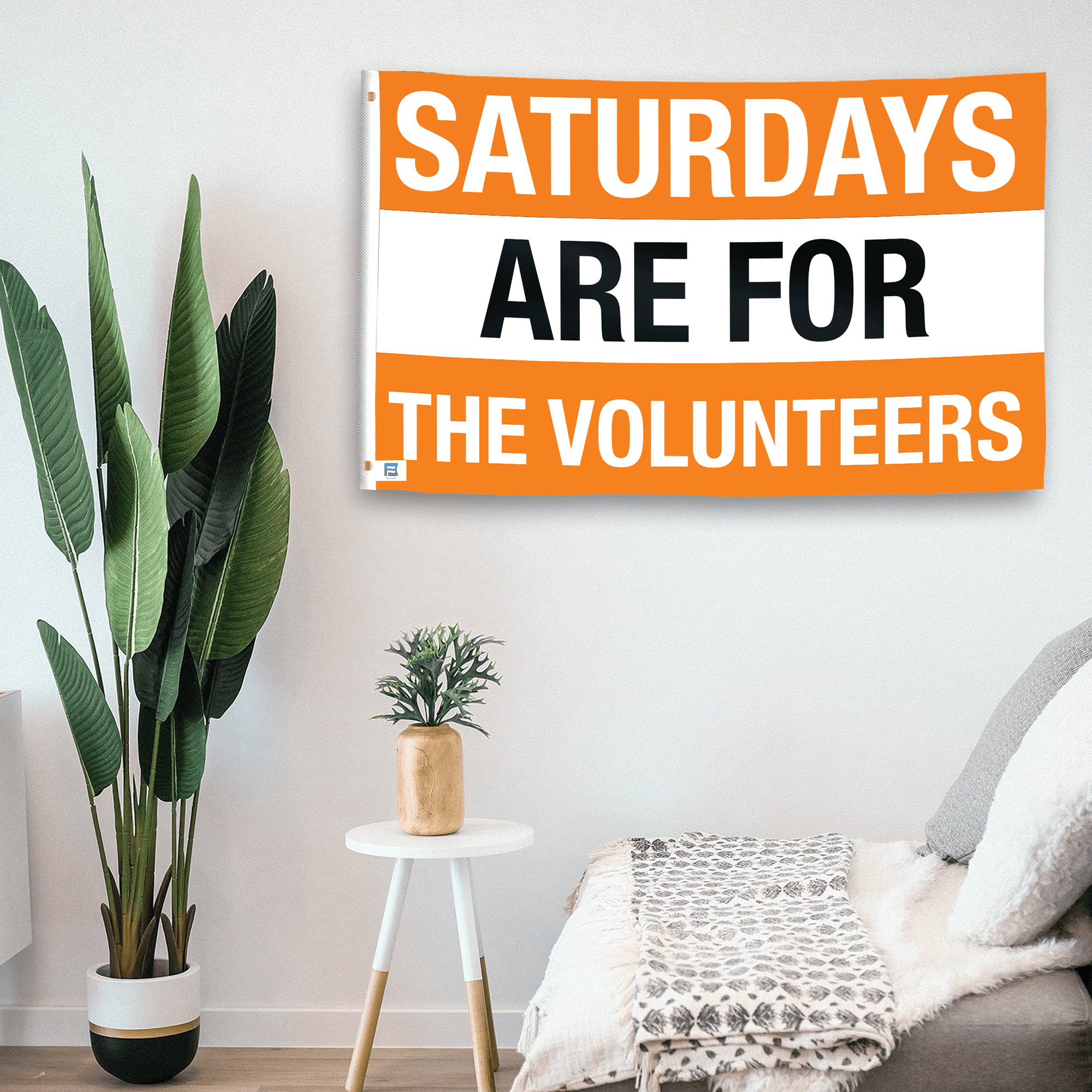 In a home setting, a flag with the saying "Saturdays Are for the Volunteers" is mounted on a white wall by a side table.