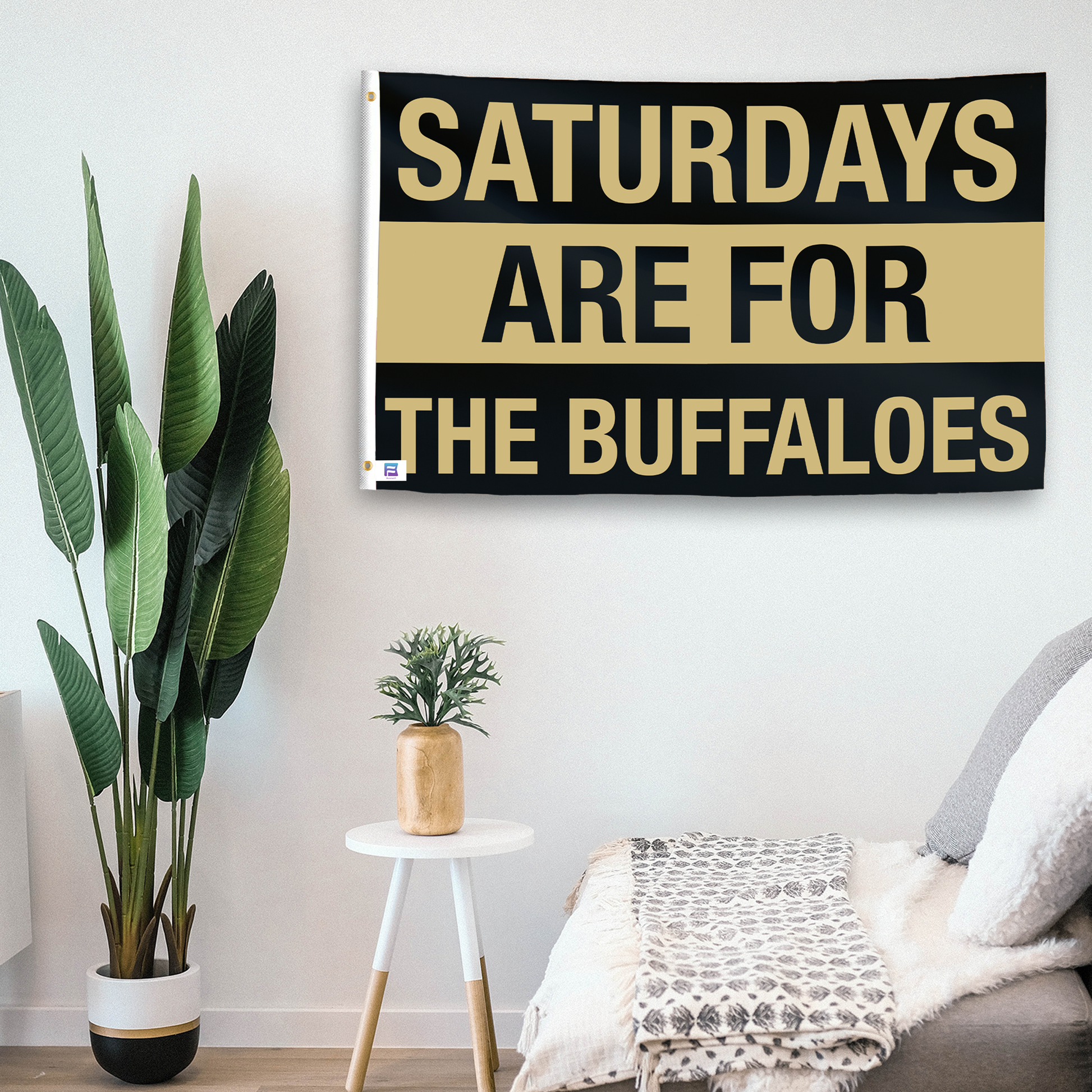 In a home setting, a flag with the saying "Saturdays Are for the Buffaloes" is mounted on a white wall by a side table.