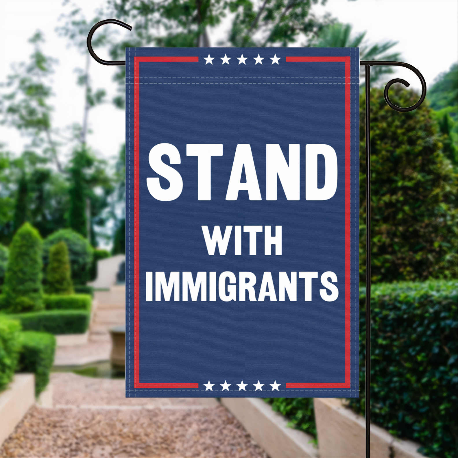 A red, white and blue political garden flag with the slogan Stand With Immigrants.