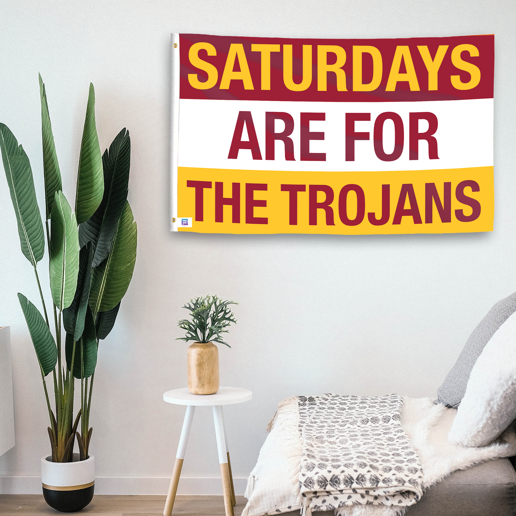 In a home setting, a flag with the saying "Saturdays Are for the Trojans" is mounted on a white wall by a side table.