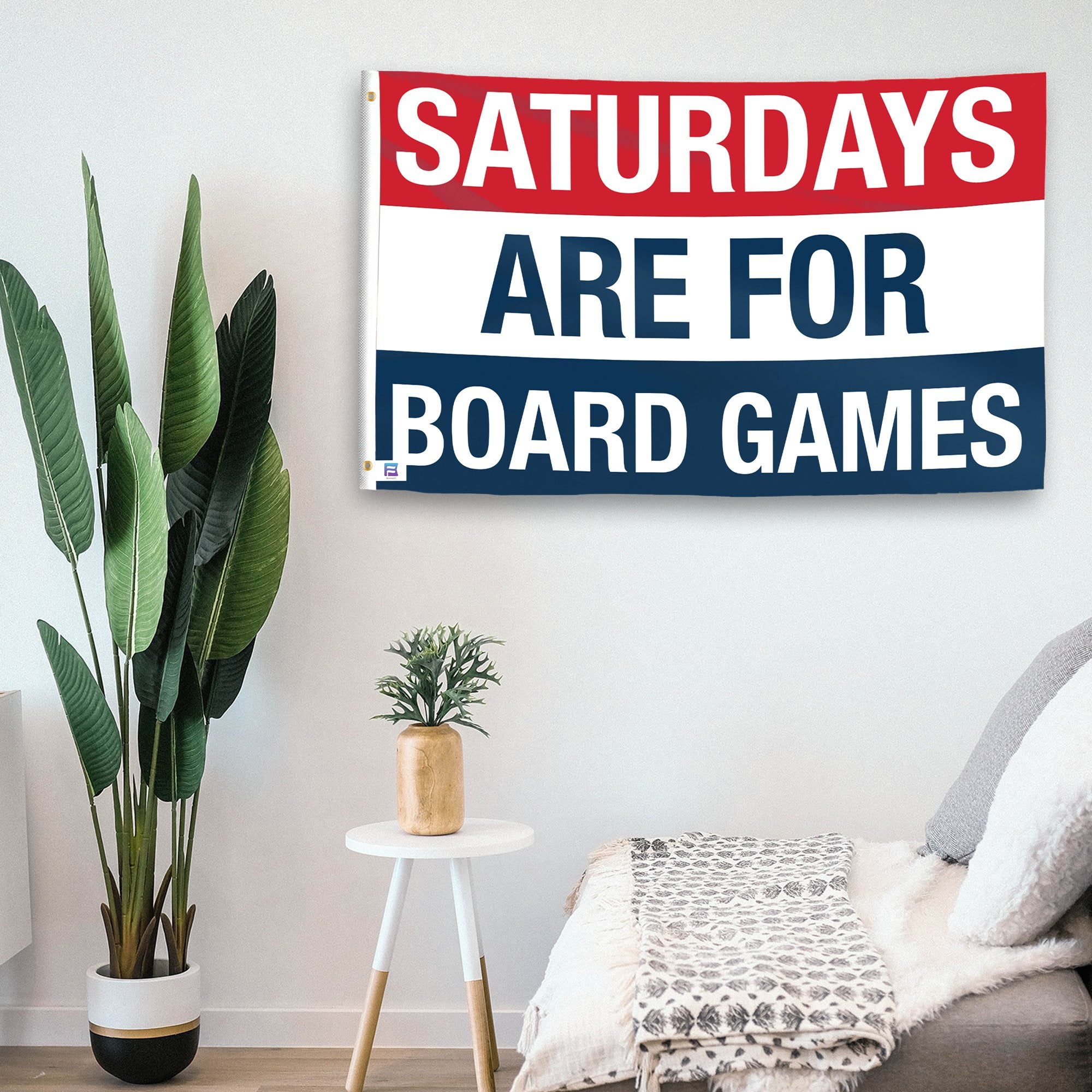 In a home setting, a flag with the saying "https://www.dropbox.com/scl/fi/tsta2xgqdw9e34i9adyc8/saturdays-are-for-board-games_room.png?rlkey=dhld5oa7m6yrodi5gro5jerbd&raw=1" is mounted on a white wall by a side table.