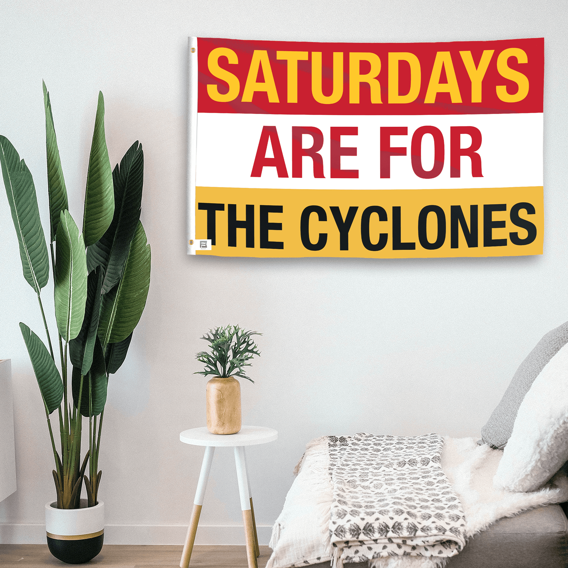 In a home setting, a flag with the saying "Saturdays Are for the Cyclones" is mounted on a white wall by a side table.