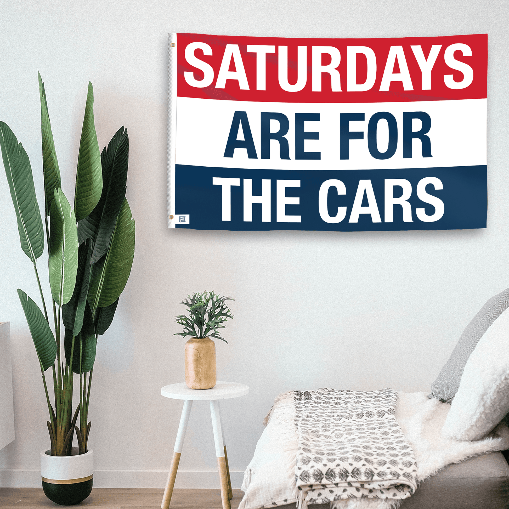 In a home setting, a flag with the saying "https://www.dropbox.com/scl/fi/zvpodko9znjjhefdx31za/saturdays-are-for-the-cars_room.png?rlkey=rbtf2q5gdjnb23oa1q9389nkl&raw=1" is mounted on a white wall by a side table.