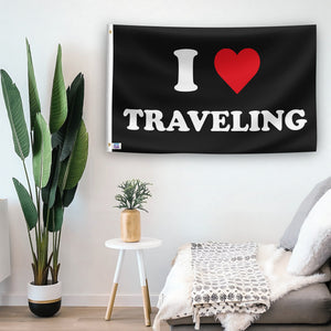 In a home setting, a flag with the saying "I Love Traveling" is mounted on a white wall by a side table.