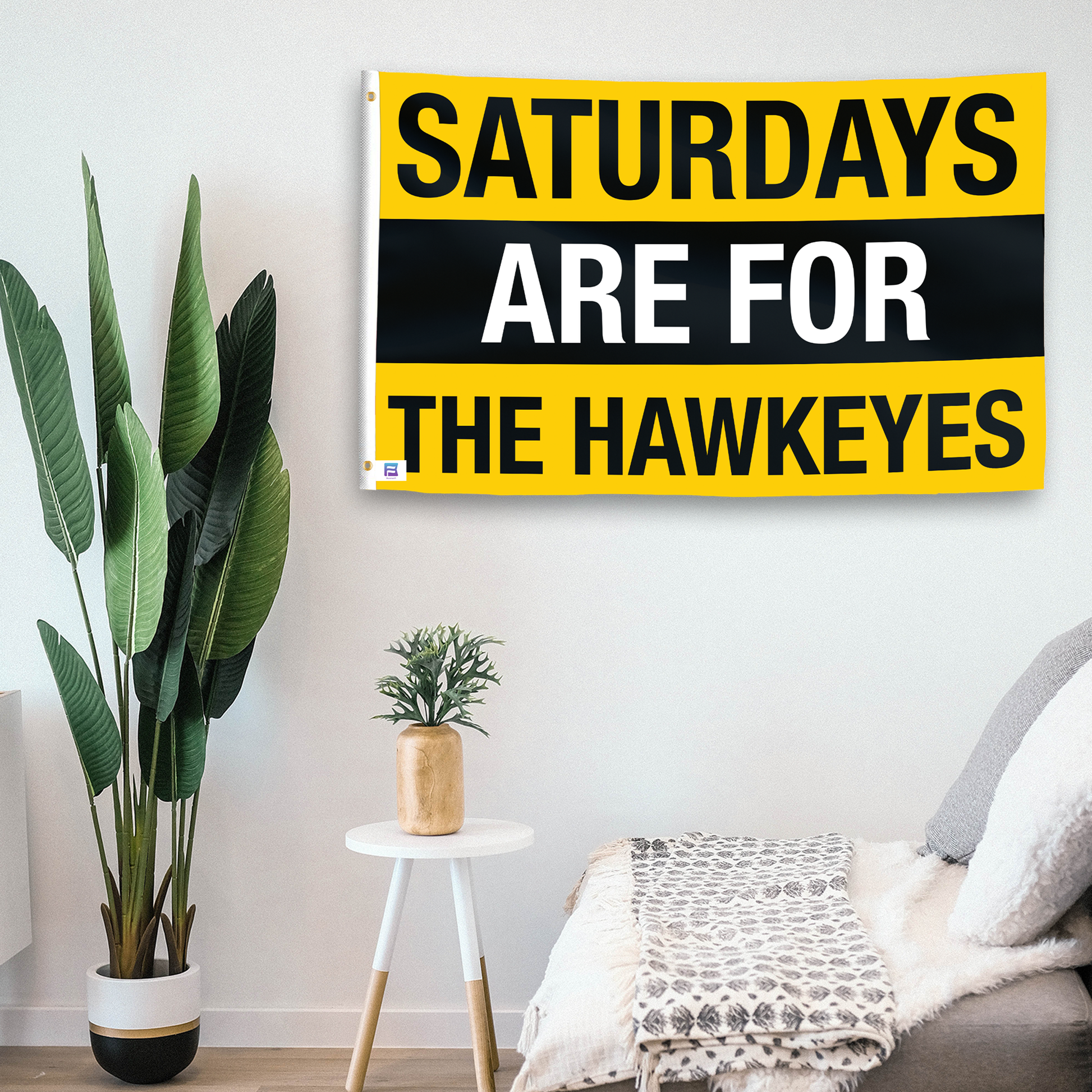 In a home setting, a flag with the saying "Saturdays Are for the Hawkeyes" is mounted on a white wall by a side table.