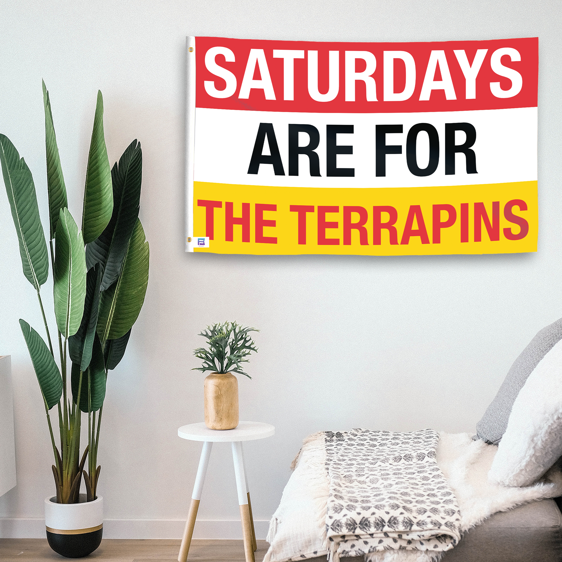 In a home setting, a flag with the saying "Saturdays Are for the Terrapins" is mounted on a white wall by a side table.