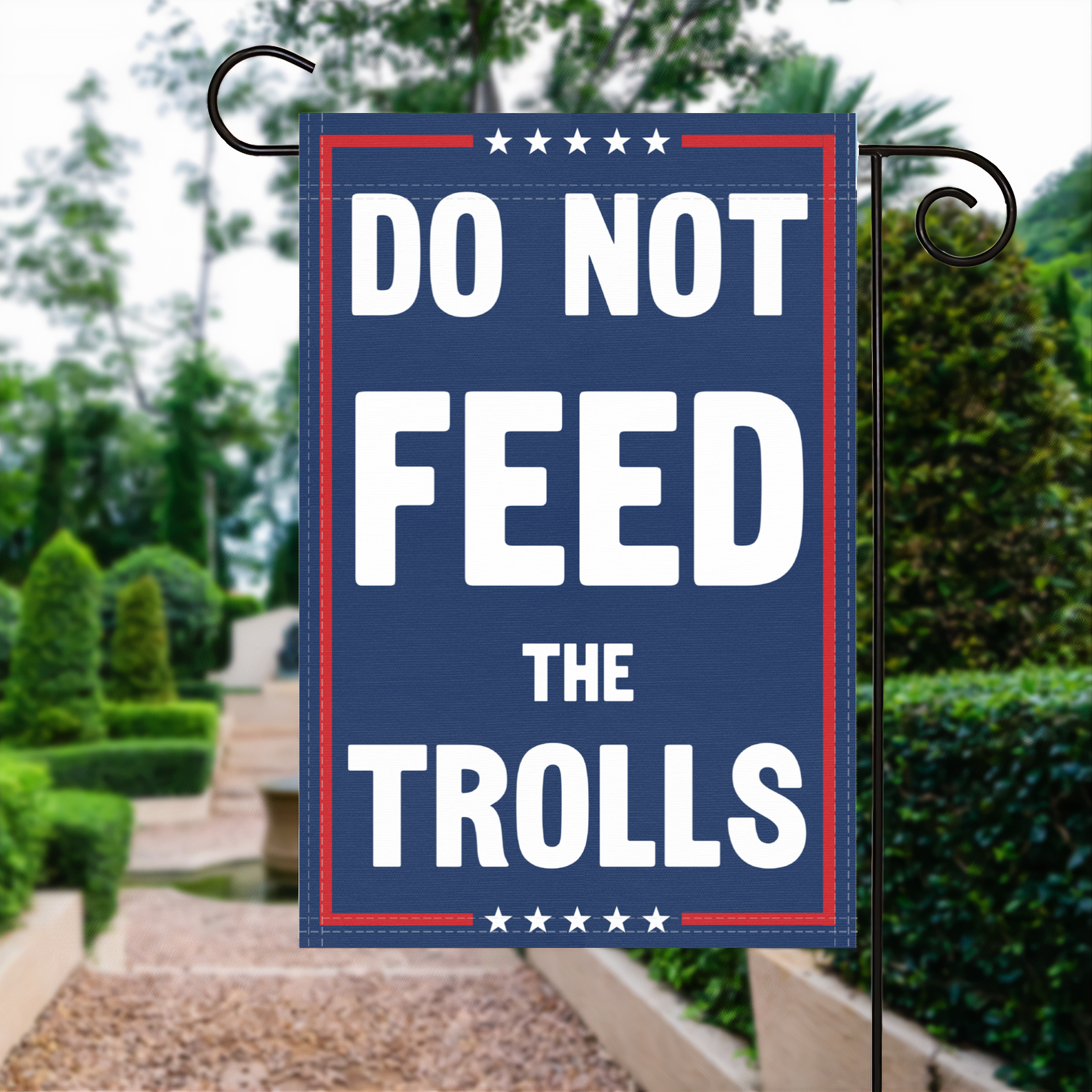 A red, white and blue political garden flag with the slogan Do Not Feed The Trolls.