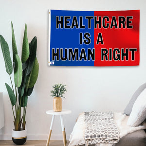 In a home setting, a blue and red flag with a political slogan is mounted on a white wall by a side table.