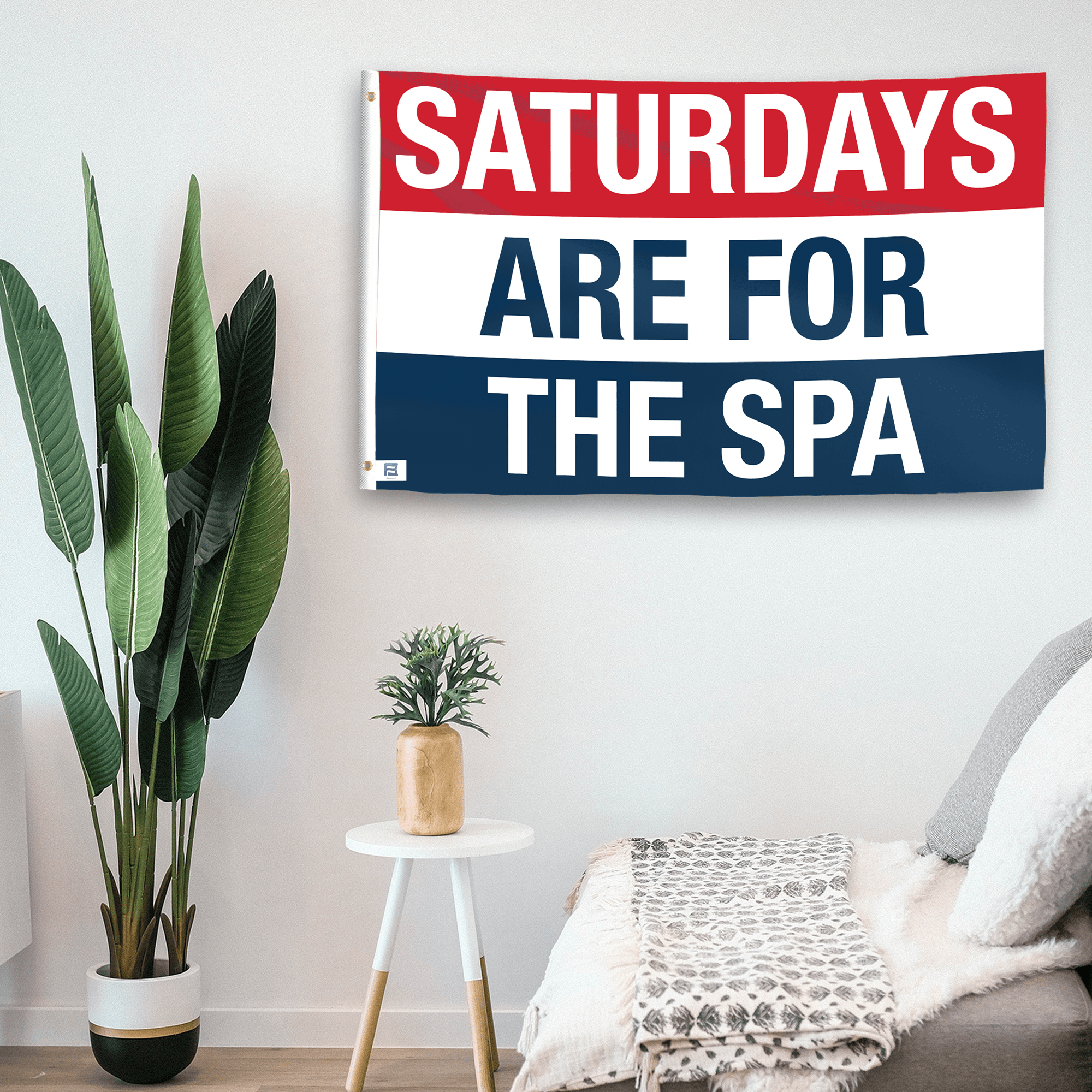 In a home setting, a flag with the saying "https://www.dropbox.com/scl/fi/xbs33qh9ylrajsdxlk6z5/saturdays-are-for-the-spa_room.png?rlkey=txogbxkyoiwddf25u37a6pwox&raw=1" is mounted on a white wall by a side table.