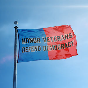 A flag containing a political slogan displayed on a high pole, featuring a patriotic red and blue background.