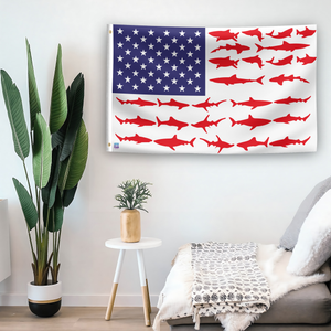 In a home setting, an american flag with the theme "Shark Stripes American" is mounted on a white wall by a side table.