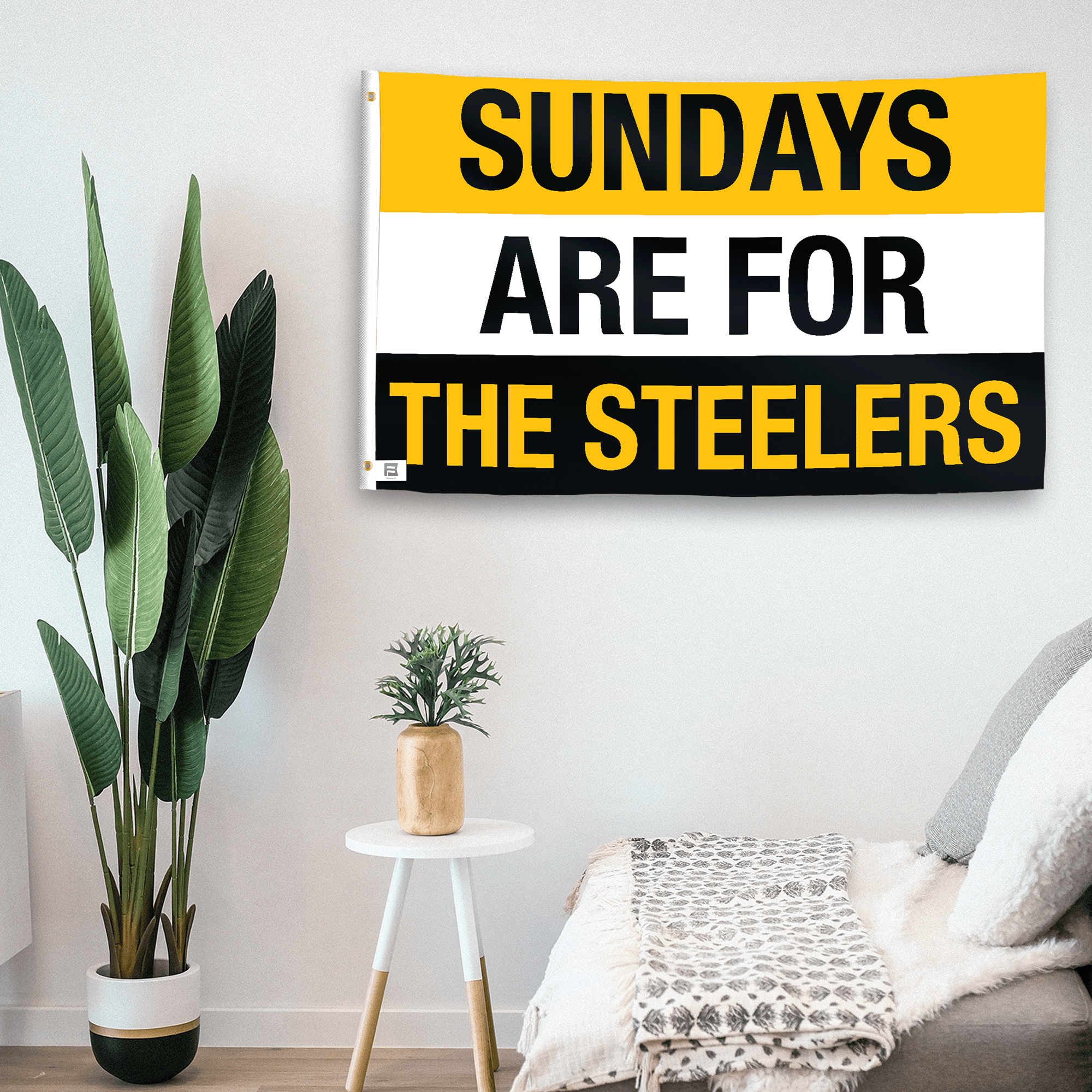 In a home setting, a flag with the saying "https://www.dropbox.com/scl/fi/mwlwj8cvtcvnzu1d9e0xh/sundays-are-for-the-steelers_room.png?rlkey=iqpzas2mkk09py4l6c1cwlkl0&raw=1" is mounted on a white wall by a side table.