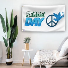 Load image into Gallery viewer, In a home setting, a flag with the saying &quot;Peace Day&quot; is mounted on a white wall by a side table.
