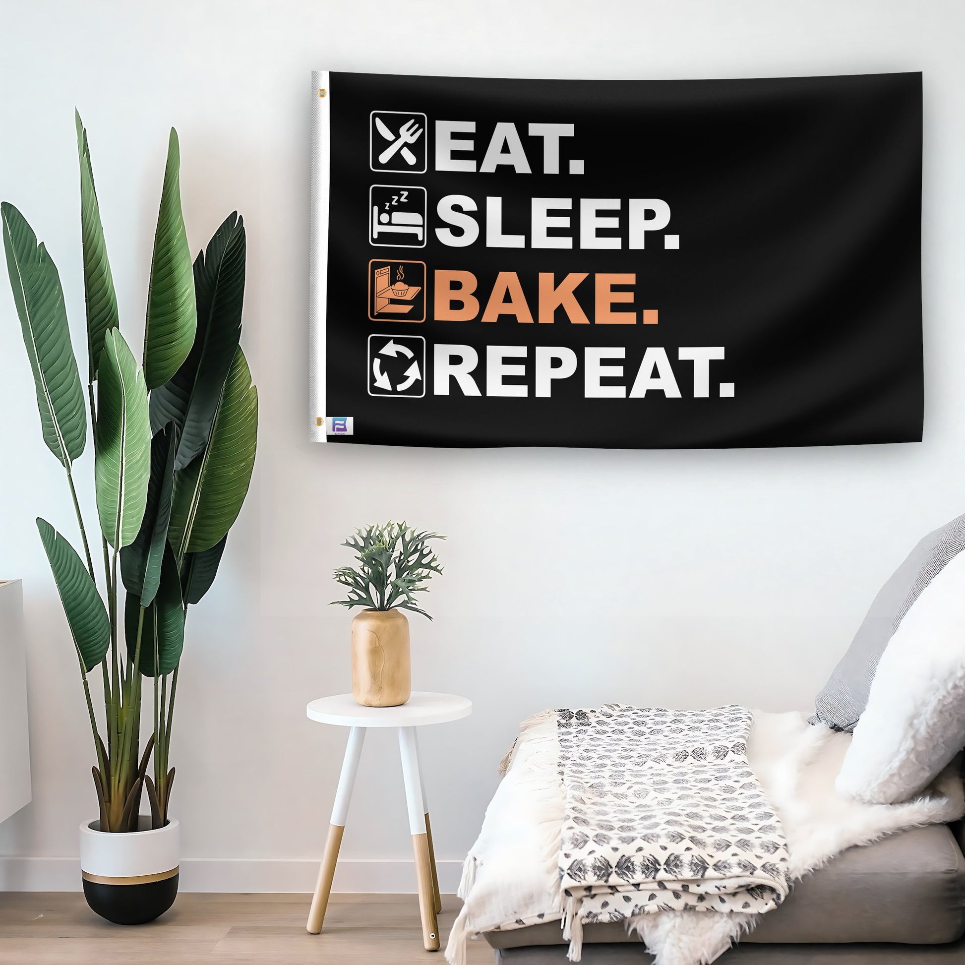 In a home setting, a flag with the saying "Eat Sleep Bake Repeat" is mounted on a white wall by a side table.