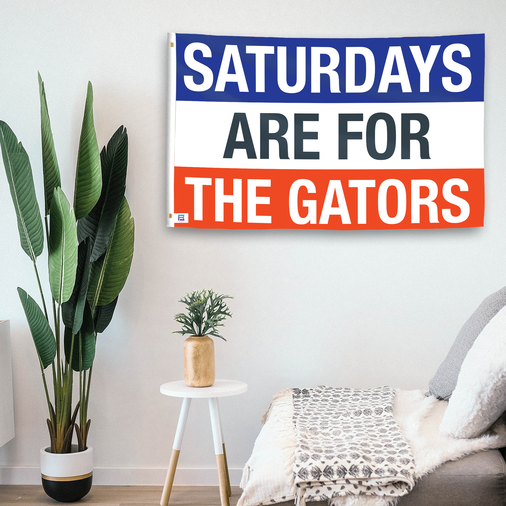 In a home setting, a flag with the saying "Saturdays Are for the Gators" is mounted on a white wall by a side table.