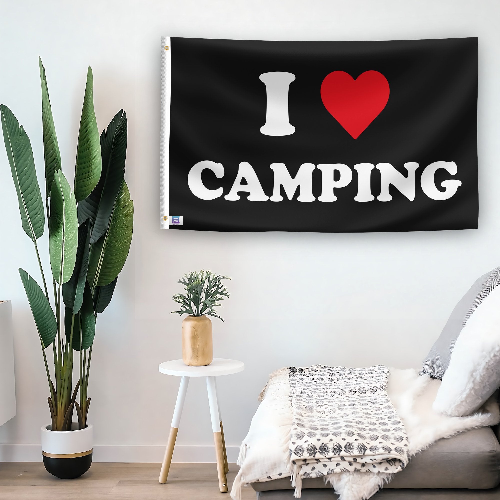 In a home setting, a flag with the saying "I Love Camping" is mounted on a white wall by a side table.