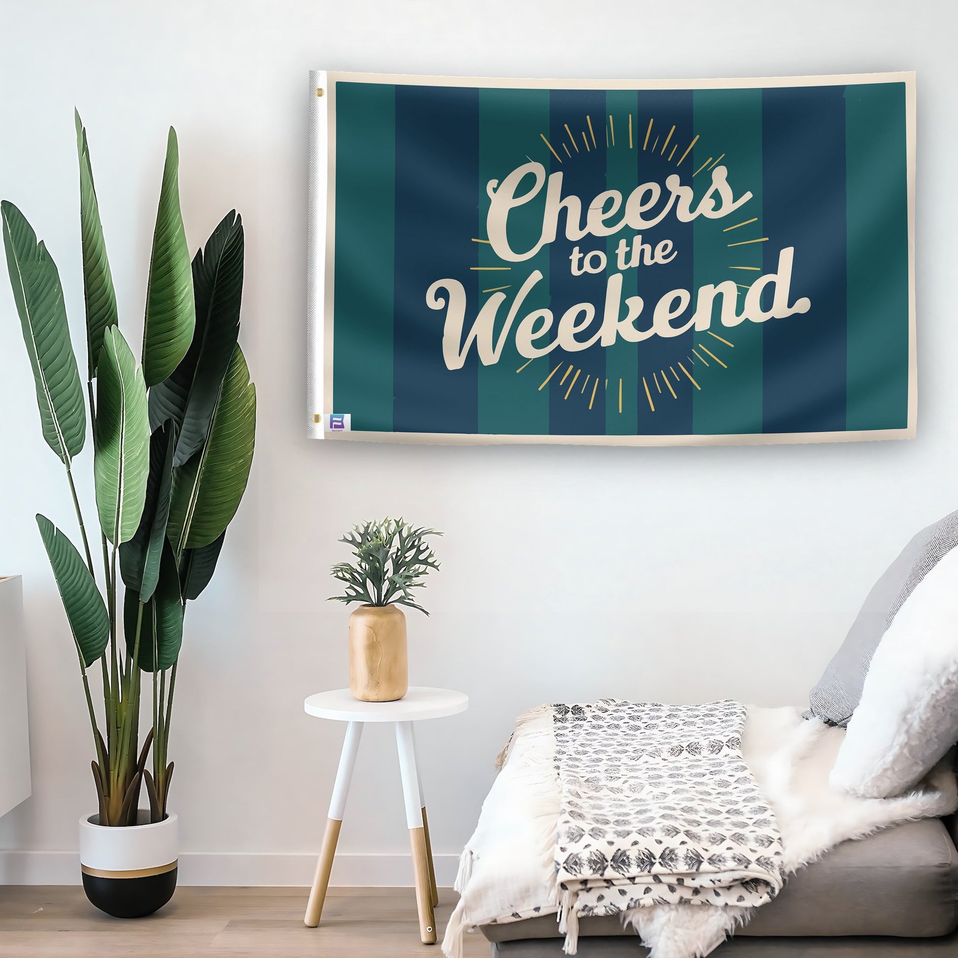 In a home setting, a flag with the saying "Cheers To The Weekend" is mounted on a white wall by a side table.