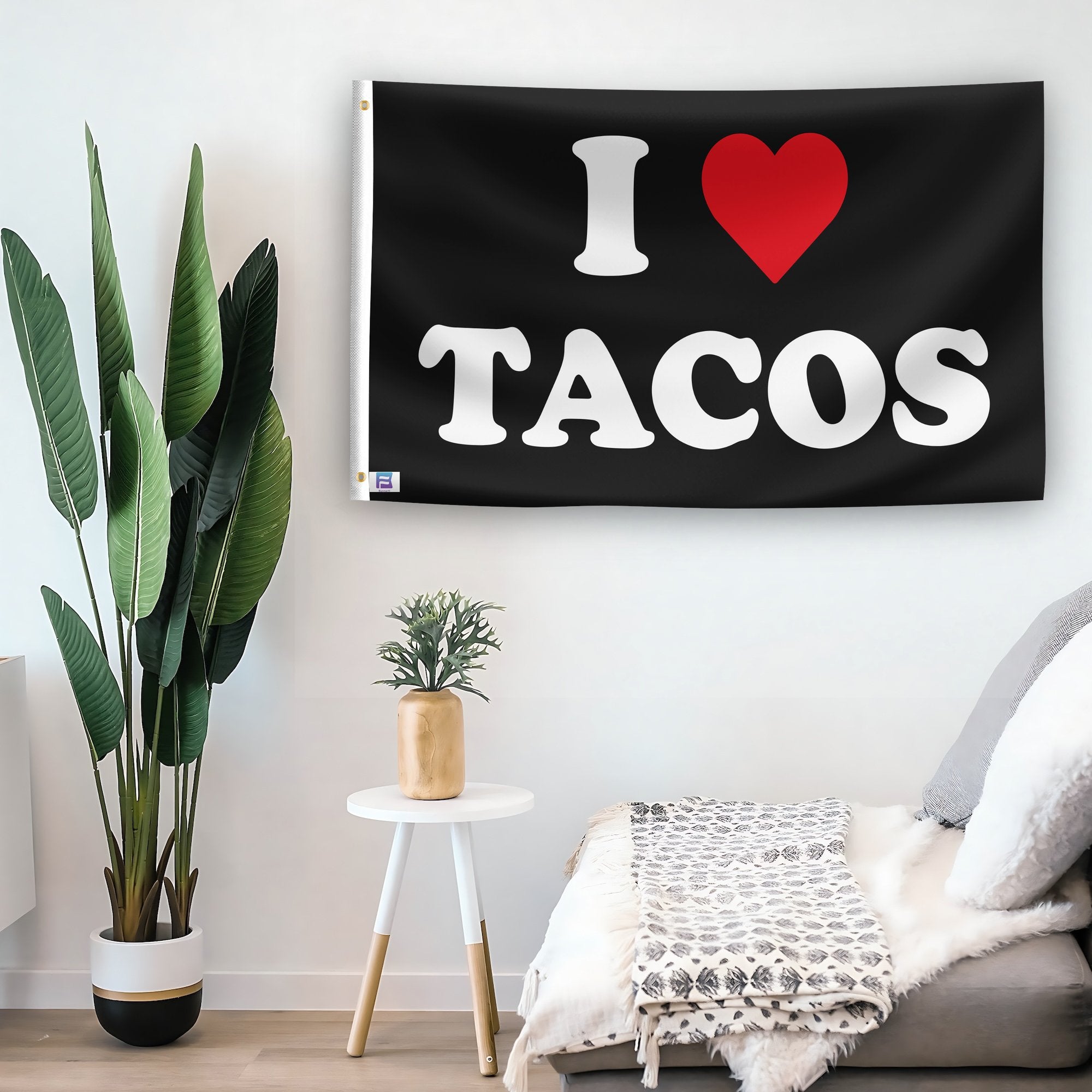 In a home setting, a flag with the saying "I Love Tacos" is mounted on a white wall by a side table.