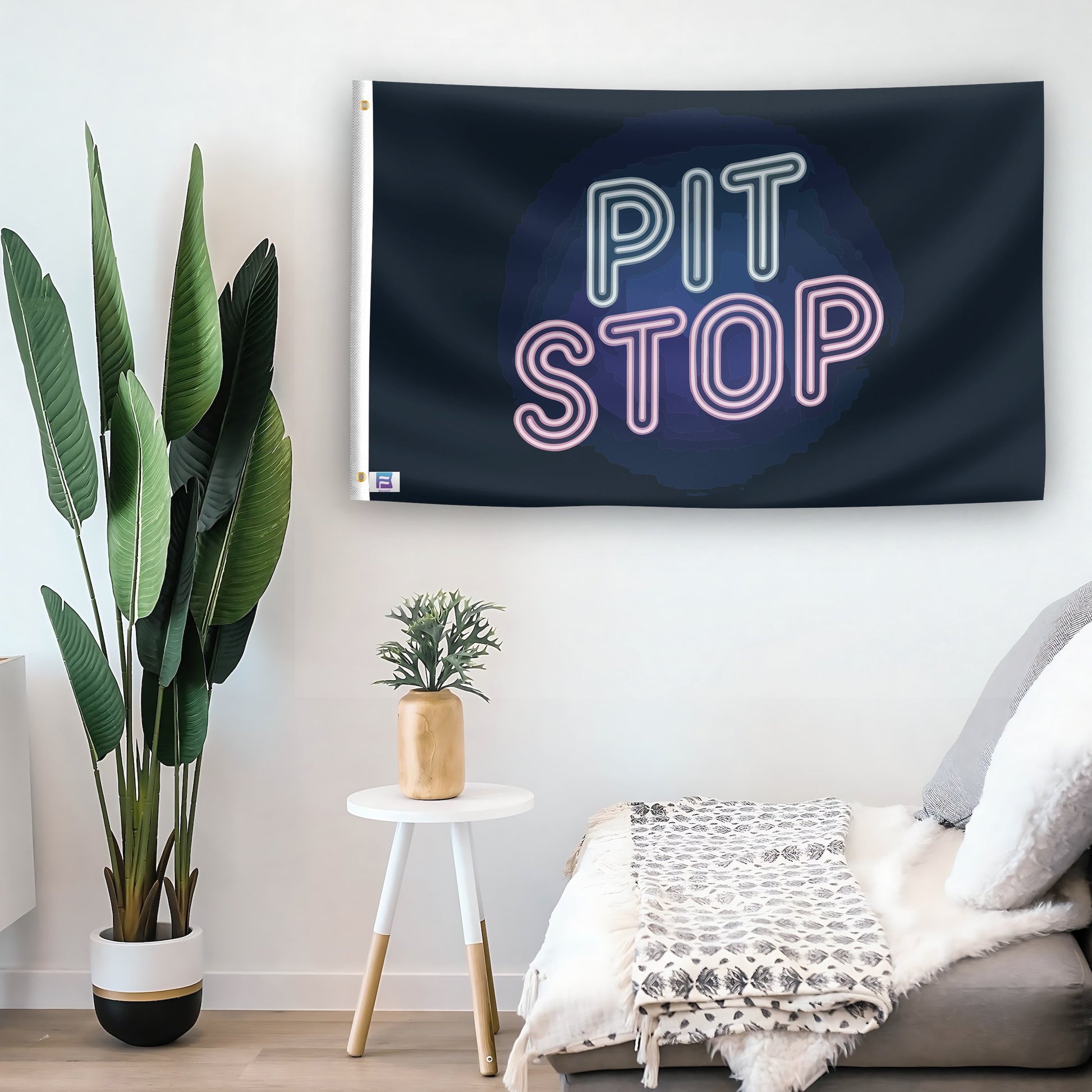 In a home setting, a flag with the saying "Pit Stop" is mounted on a white wall by a side table.