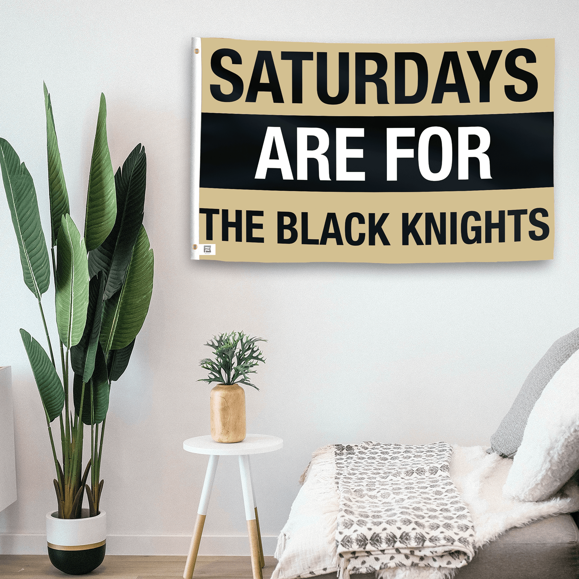 In a home setting, a flag with the saying "Saturdays Are for the Black Knights" is mounted on a white wall by a side table.