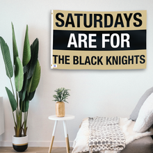 Load image into Gallery viewer, In a home setting, a flag with the saying &quot;Saturdays Are for the Black Knights&quot; is mounted on a white wall by a side table.
