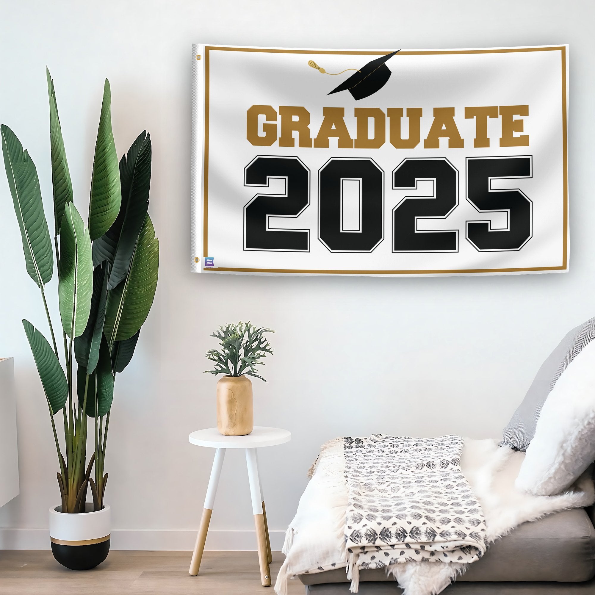 In a home setting, a flag with the saying "Graduate 2025" is mounted on a white wall by a side table.