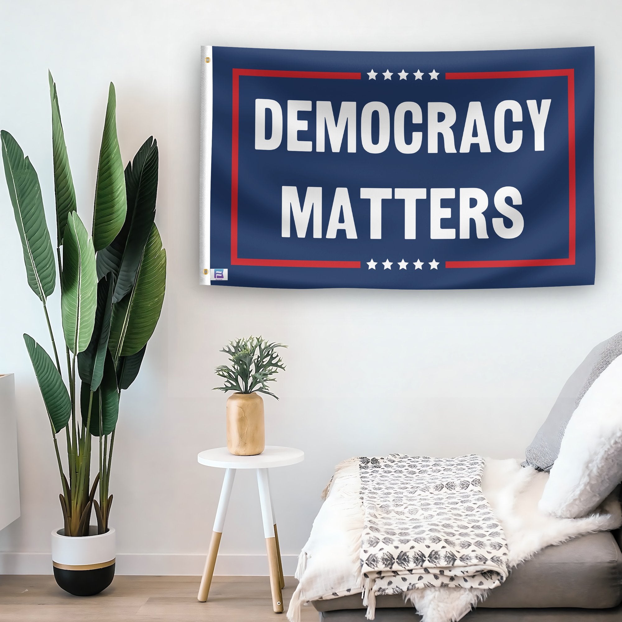 In a home setting, a flag with the saying "Democracy Matters Political" is mounted on a white wall by a side table.