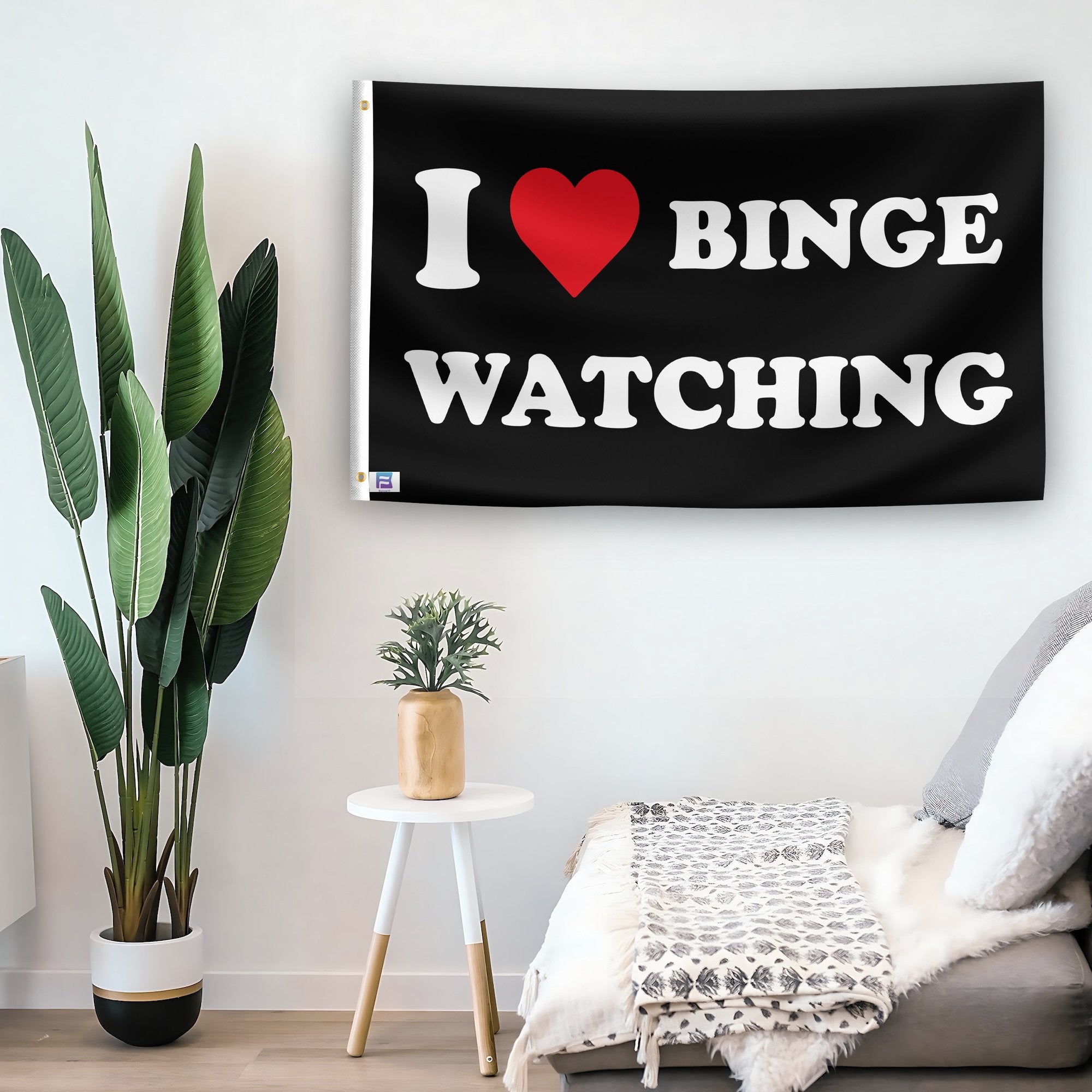 In a home setting, a flag with the saying "I Love Binge Watching" is mounted on a white wall by a side table.