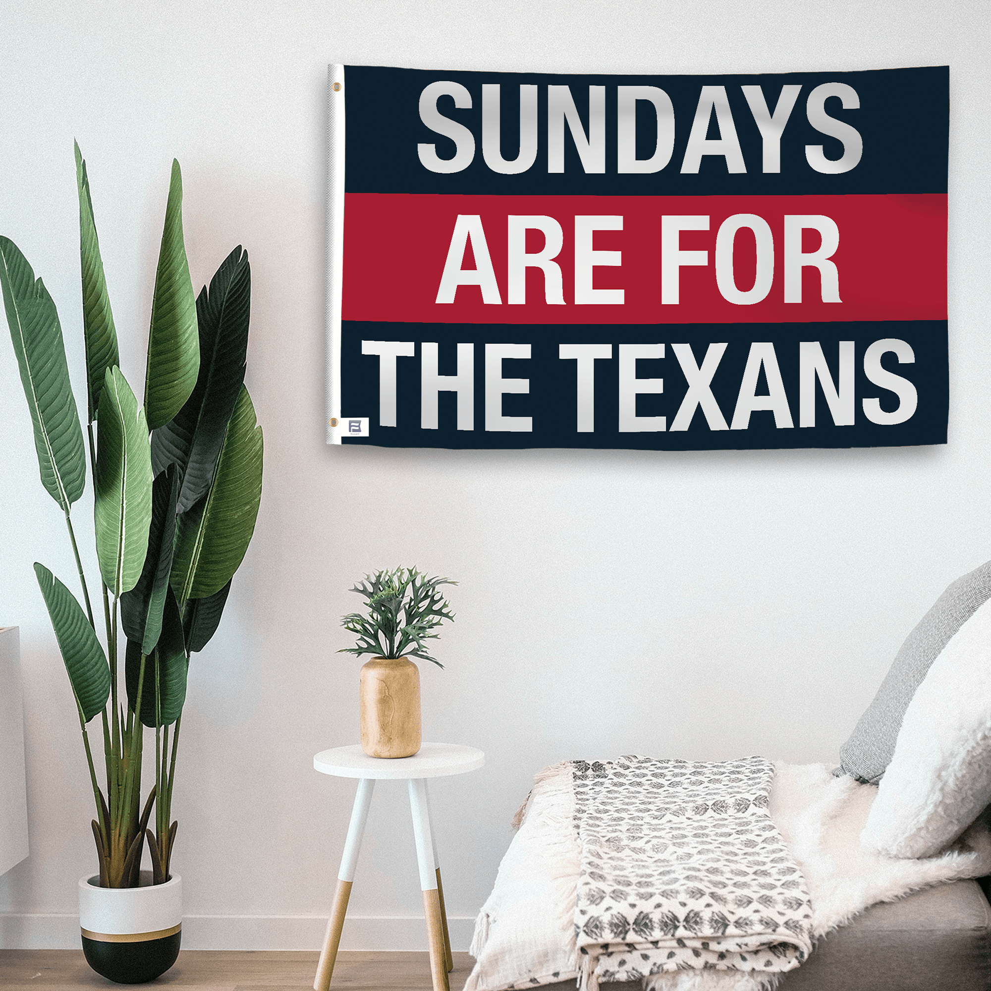 In a home setting, a flag with the saying "https://www.dropbox.com/scl/fi/8sc9usri6w0edd18fze0y/sundays-are-for-the-texans_room.png?rlkey=tjgb7n3jofh3c127zh8s0twrj&raw=1" is mounted on a white wall by a side table.