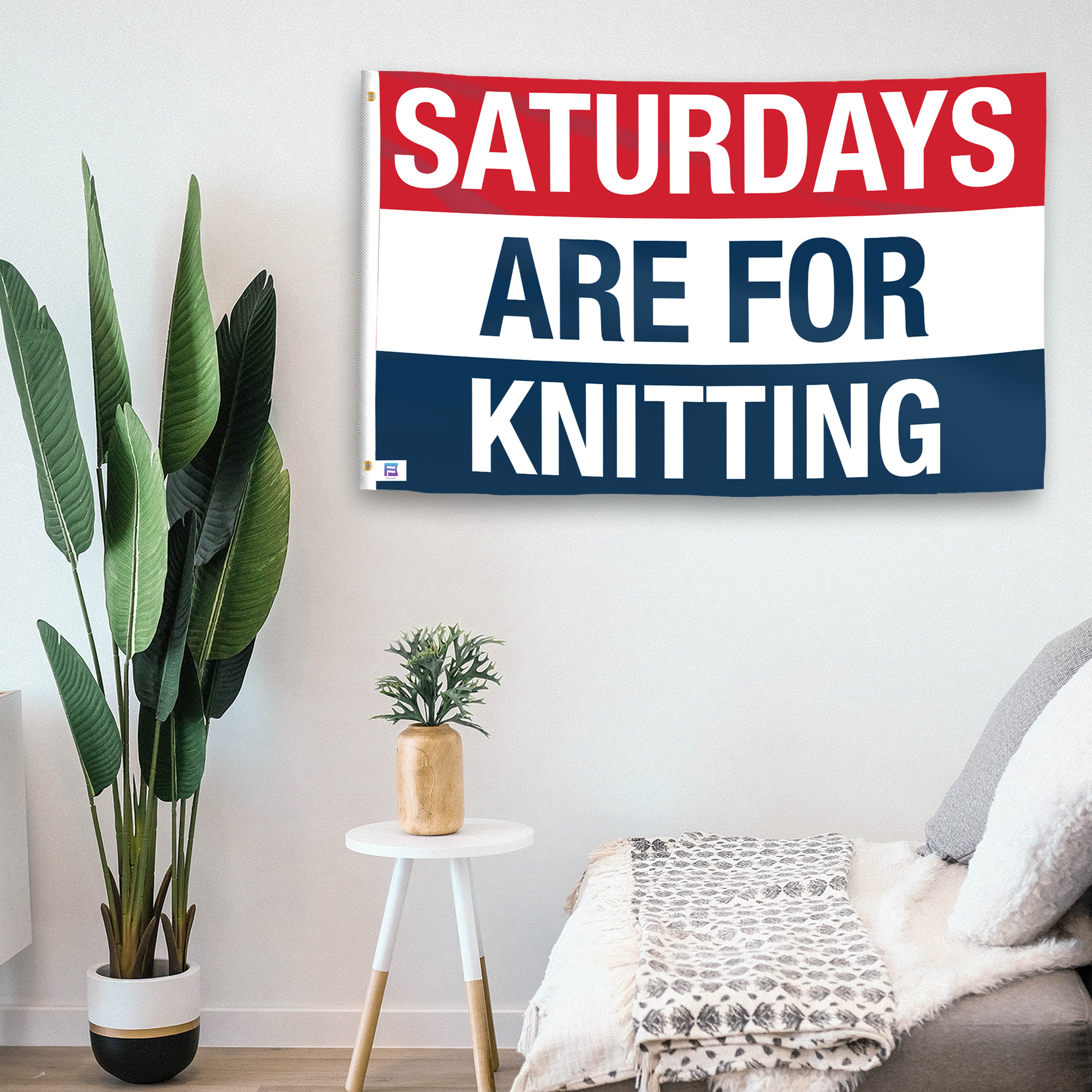 In a home setting, a flag with the saying "https://www.dropbox.com/scl/fi/reeedkvtbn9jxqbrgkh2t/saturdays-are-for-knitting_room.png?rlkey=ms8vs3ifa0t1ijzc4gfppnnwn&raw=1" is mounted on a white wall by a side table.