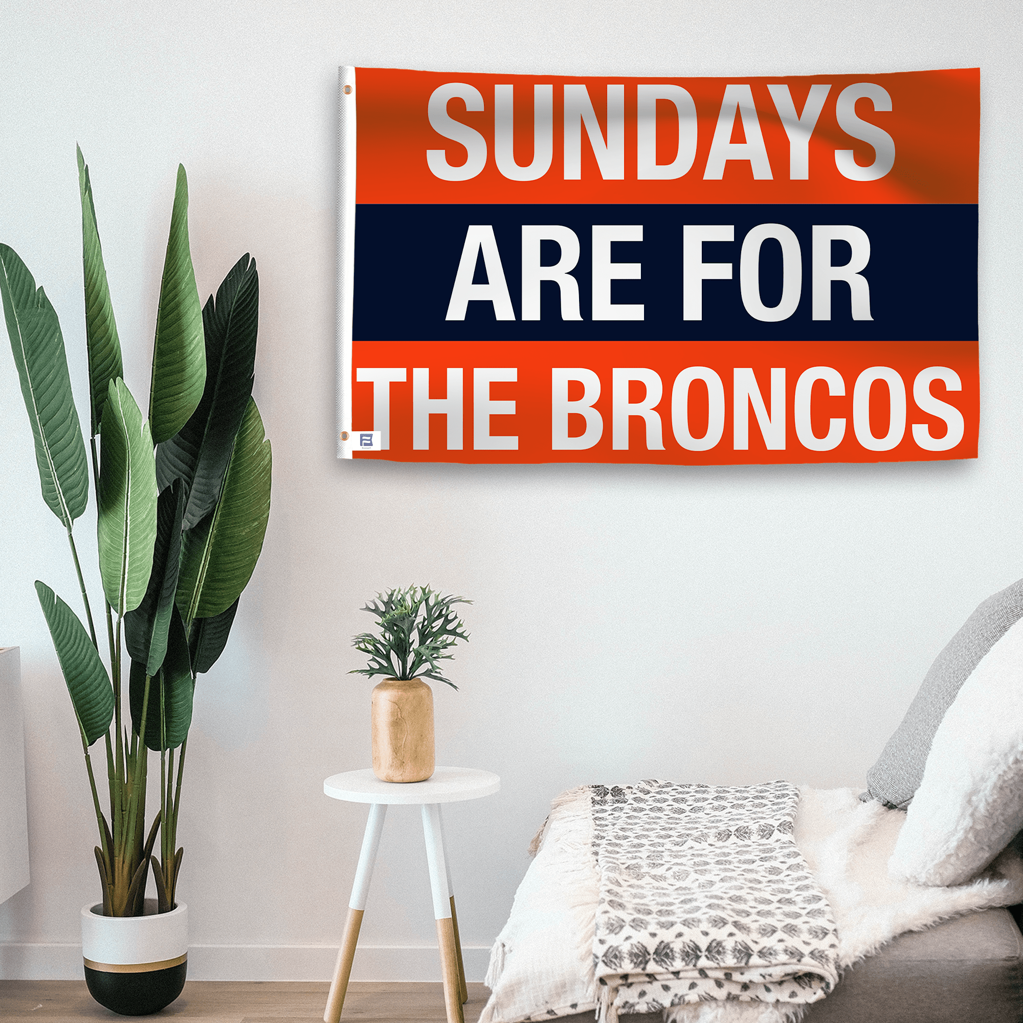 In a home setting, a flag with the saying "https://www.dropbox.com/scl/fi/zd3ft13n68b9lr6rptvai/sundays-are-for-the-broncos_room.png?rlkey=o7bntbbew4h427efcn45fx3on&raw=1" is mounted on a white wall by a side table.