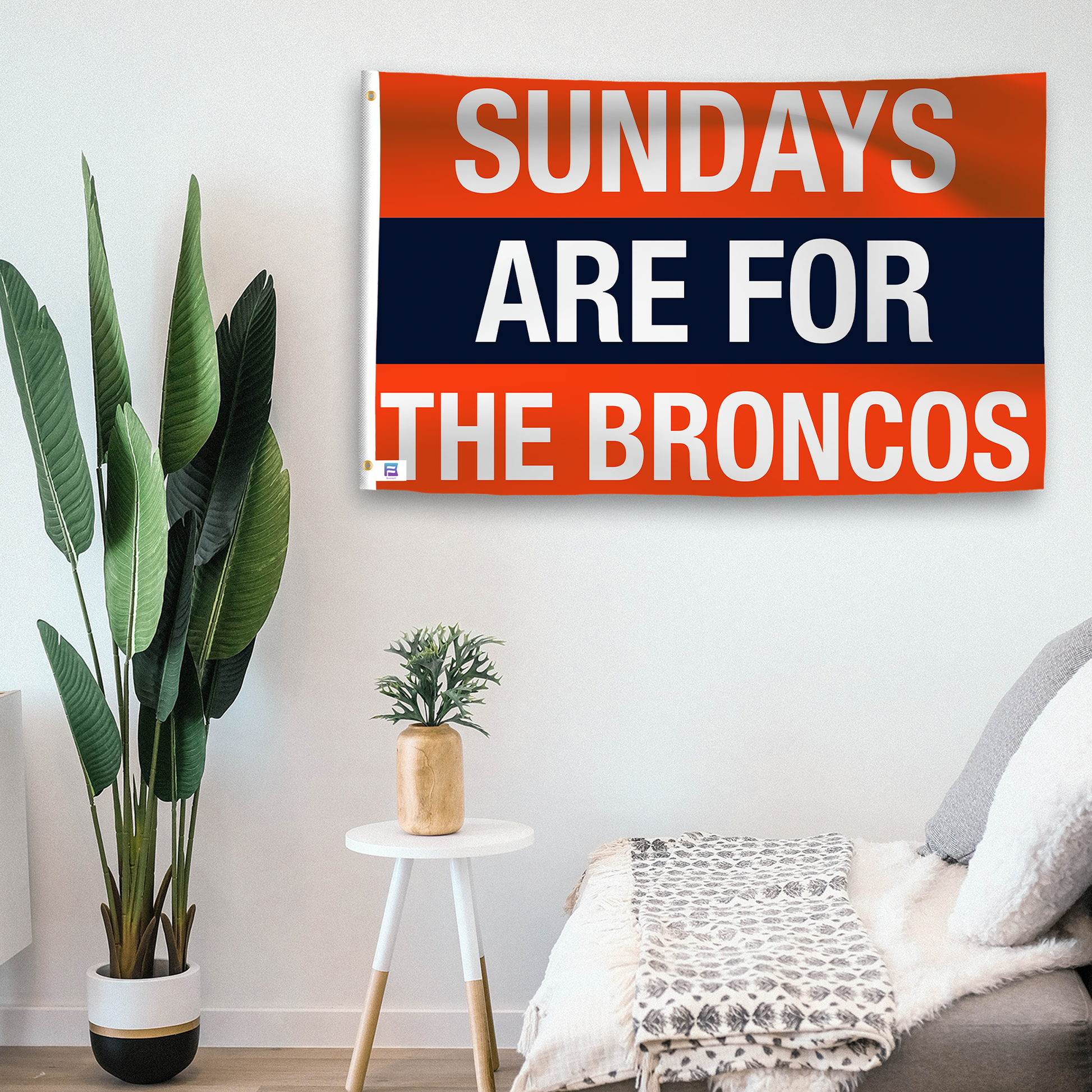 In a home setting, a flag with the saying "https://www.dropbox.com/scl/fi/zd3ft13n68b9lr6rptvai/sundays-are-for-the-broncos_room.png?rlkey=o7bntbbew4h427efcn45fx3on&raw=1" is mounted on a white wall by a side table.