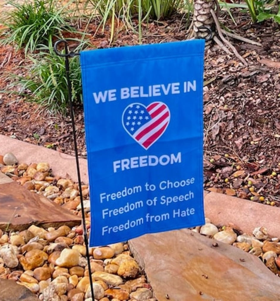 Blue garden flag with text and heart design on a garden background