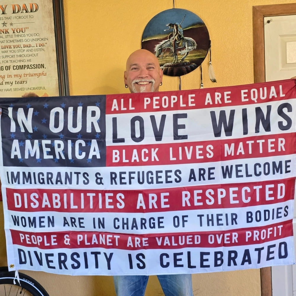 Person holding a banner with social justice messages in a room with a yellow wall and framed picture.